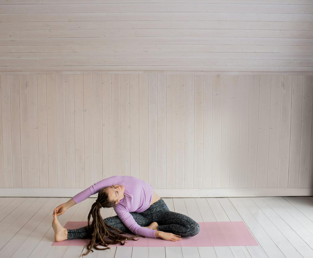 Woman with dreadlocks doing yoga indoors, demonstrating flexibility and relaxation.